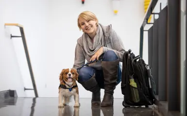 female student smiling and squatting next to a small service dog