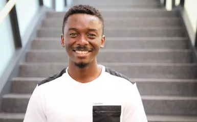 biology alumni Afeez Sodeinde standing in the grand hall of the center for business and technology smiling and facing the camera