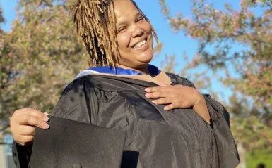 student to faculty member Audua Pugh in her graduation gown in the NHCC courtyard