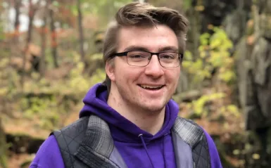 student Josh Betterman standing outside in a forest smiling for the camera