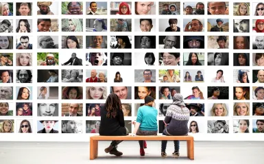 Image of students on a bench looking at photos on a wall. 