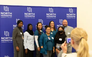 a photo of a photo being taken in front of an NHCC backdrop at the scholarship reception with Dr. Garcia