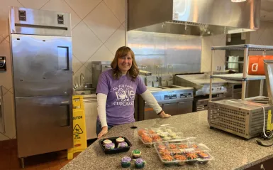 a photo of NHCC math faculty, Deane Newborg in the Campus Center kitchen with the cupcakes she baked. 