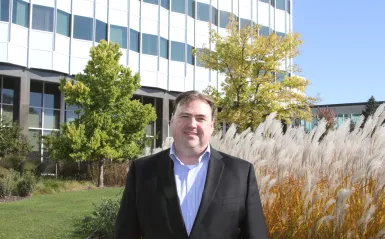 a photo of Michael Larson, NHCC Paralegal Alumni in a suit, smiling, outside of the 3M headquarters office building