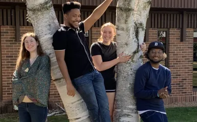 Four students from the Creative Writing Club pose outside of the HWC building next to a tree. 