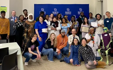 This is a group photo of various students and staff who attended the Student Life Awards Banquet. The group piled together for a photo in front of the NHCC logo backdrop. 