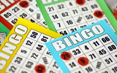 This is a photo of four colorful bingo sheets on top of each other with various red circular chips lined up on the bingo cards. 