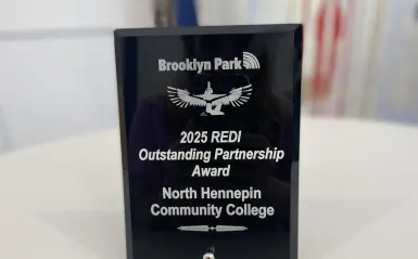 this is a photo of an award sitting on a table. The award was given to NHCC from the City of Brooklyn Park. It was the 2025 REDI Outstanding Partnerships Award. 