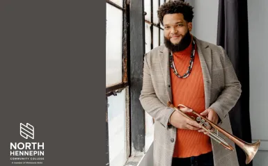 this is a headshot photo of jazz musician, Kris Johnson holding his trumpet and standing near a window.  