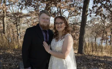 this is a wedding photo of Theo and Maddi, two NHCC alumni posing together outside, smiling on their special day. 