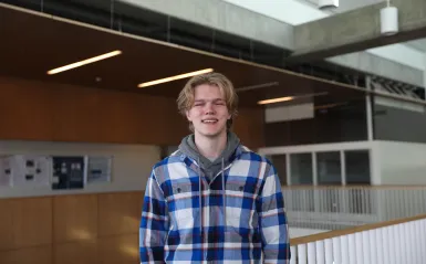 this is a photo of former NHCC student, Casey Hjelmstad, standing near the top of the staircase in NHCC's BHCC building, smiling at the camera. 