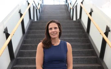 this is a smiling photo of NHCC graduate, Kari Struble, standing in front of a staircase in the CBT building. 