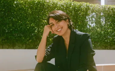 Person with dark hair sitting outside smiling on a sunny day. 