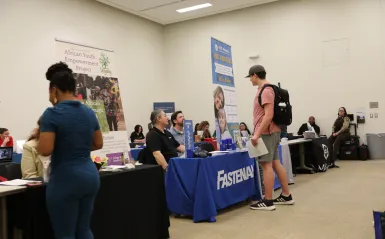 this is a photo of two students visiting with employers at tables at a Career Fair in Helling Hall at NHCC. 