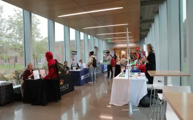 this is a photo of the BHCC hallway during a Career Fair with tables set up on either side of the hall, with students walking and stopping to ask questions to the employers sitting behind the tables.