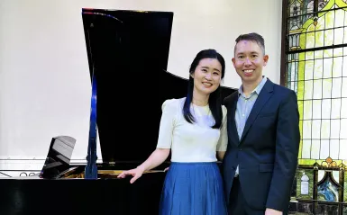 this is a smiling photo of NHCC music faculty, Grace Choi and Kevin Hobbs standing next to a piano. 