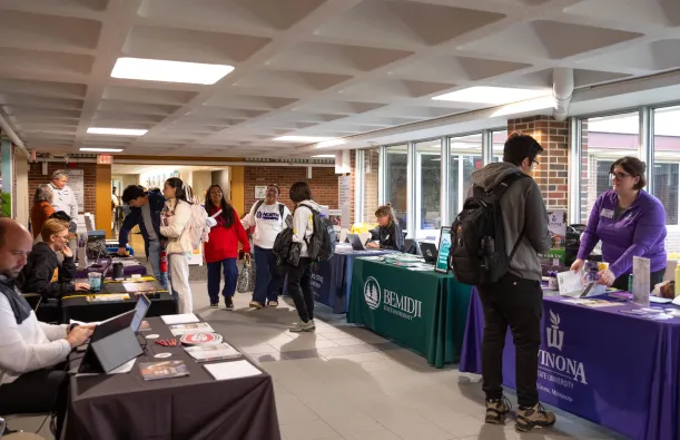 This is a photo of students walking through the ES and LRC hallway mingling with representatives from four-year colleges who are sitting there at tables in the hall to tell students about the transfer process. 