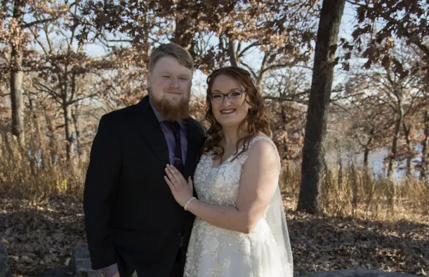 this is a wedding photo of Theo and Maddi, two NHCC alumni posing together outside, smiling on their special day. 