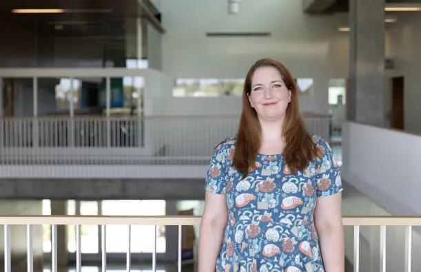this is a photo of female NHCC student, Jenny Victory, standing in the upstairs hall of the BHCC building, smiling, wearing a short sleeved dress with science illustrations on it. 