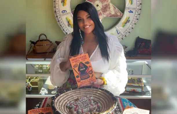 this is a smiling photo of a special guest and female author, Marique Moss. She is holding up a copy of her book, with the title reading, SweetGrass and Soul Food. 