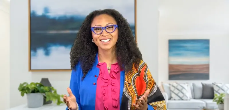 Woman wearing bright colors smiling and gesturing with open arms 