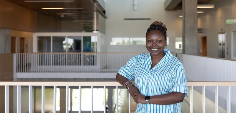 woman leaning on a railing smiling with a large open area and hallway in the background.