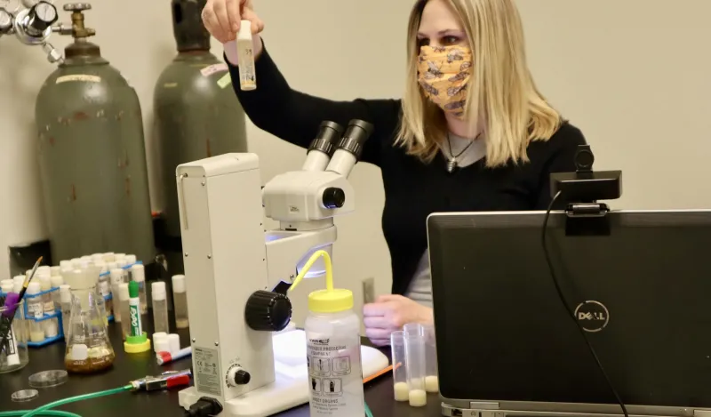 nursing student Melissa Sawyer standing in front of a microscope holding up a vial