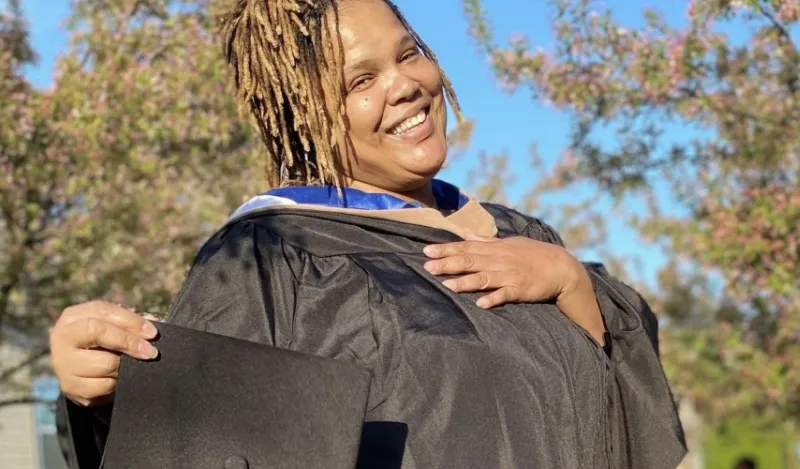 student to faculty member Audua Pugh in her graduation gown in the NHCC courtyard