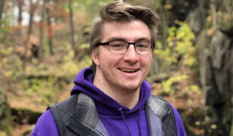 student Josh Betterman standing outside in a forest smiling for the camera