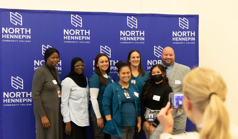 a photo of a photo being taken in front of an NHCC backdrop at the scholarship reception with Dr. Garcia