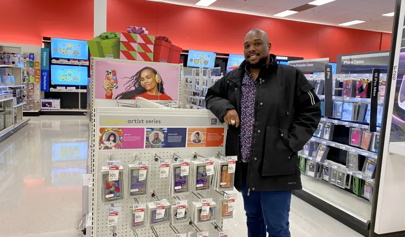 a photo of NHCC graduate, Ameen Taahir, standing next to a display at Target featuring his product designs