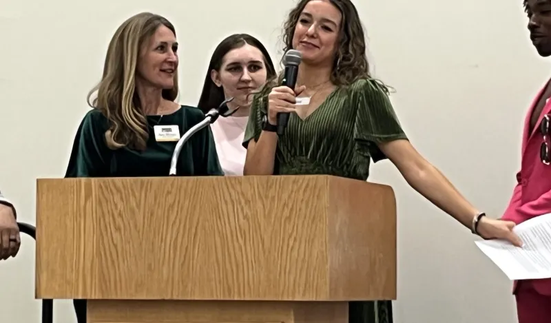 a student in a green dress speaking in the grand hall 