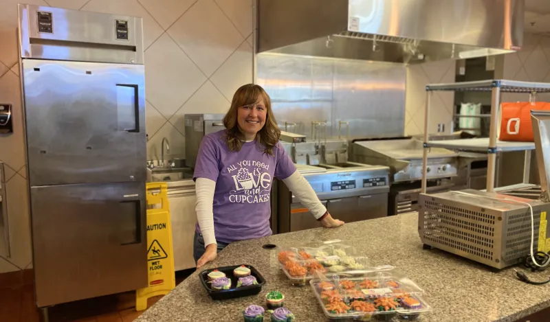 a photo of NHCC math faculty, Deane Newborg in the Campus Center kitchen with the cupcakes she baked. 