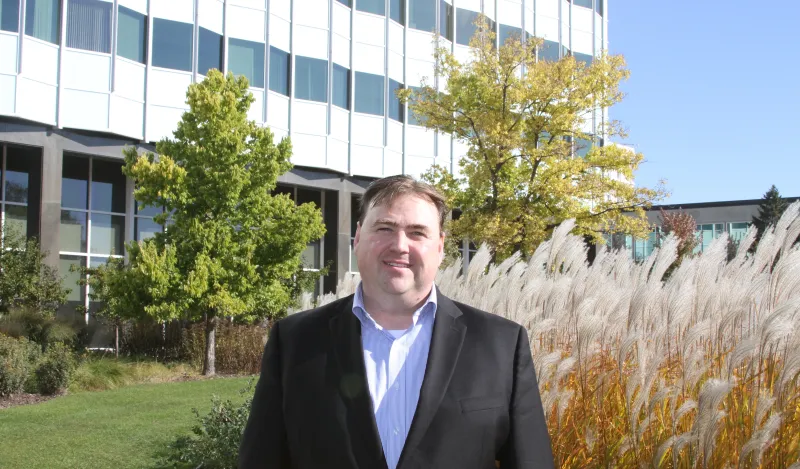 a photo of Michael Larson, NHCC Paralegal Alumni in a suit, smiling, outside of the 3M headquarters office building