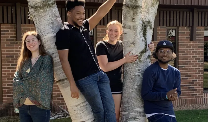Four students from the Creative Writing Club pose outside of the HWC building next to a tree.