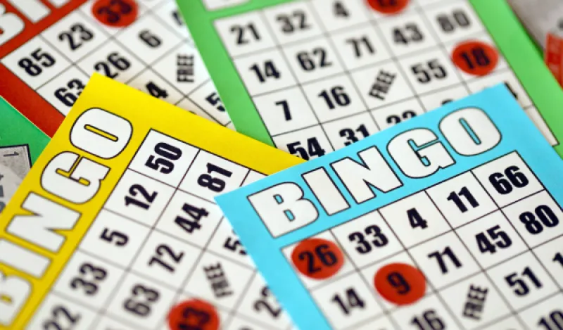 This is a photo of four colorful bingo sheets on top of each other with various red circular chips lined up on the bingo cards. 