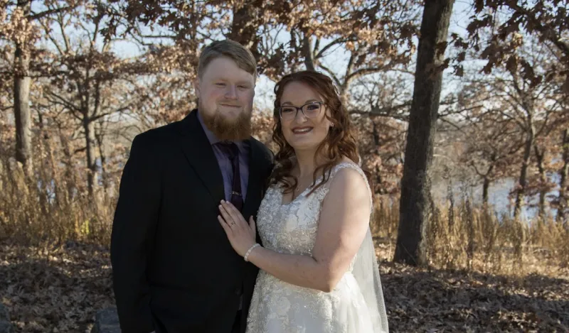 this is a wedding photo of Theo and Maddi, two NHCC alumni posing together outside, smiling on their special day. 