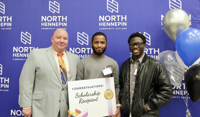 Scholarship recipients with college President Dr. Rolando Garcia holding scholarship certificate in front of backdrop