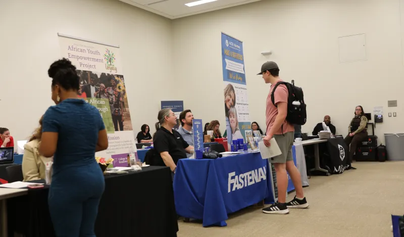 this is a photo of two students visiting with employers at tables at a Career Fair in Helling Hall at NHCC. 