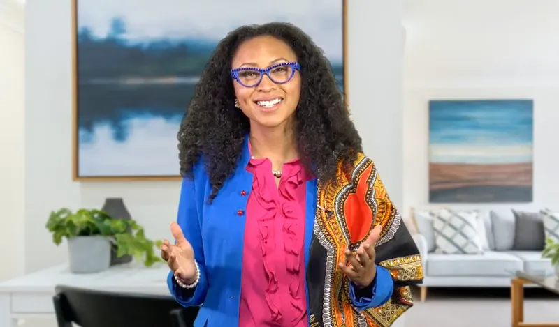 Woman wearing bright colors smiling and gesturing with open arms 