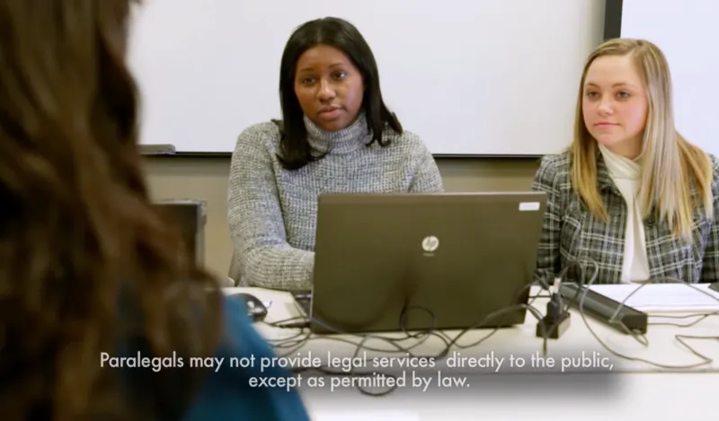 two female students with a laptop speaking to someone across a table 