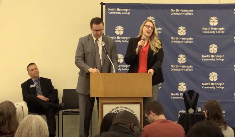 woman and man standing at podium addressing a gathered crowd