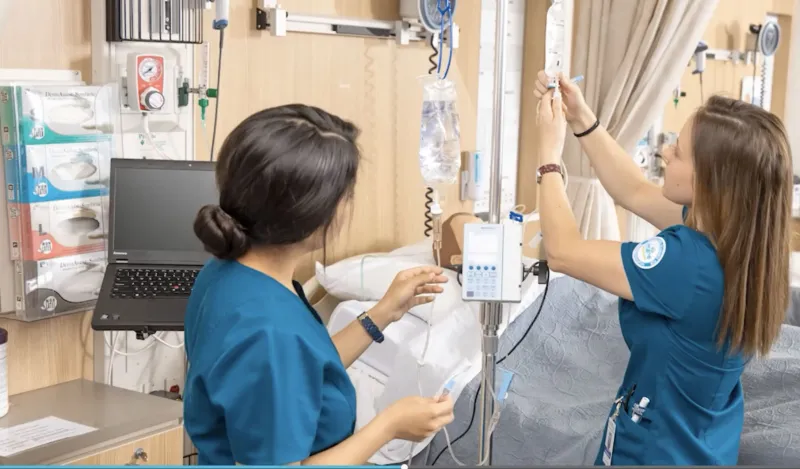 This is a photo of two female nursing students practicing with a mannequin patient. 