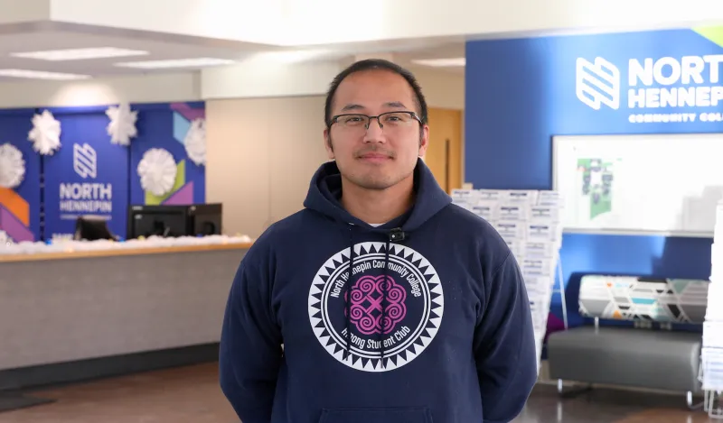 man with glasses smiling with the admissions desk in the background. 