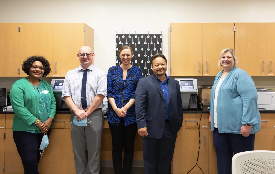 Dr. Julia Ugorji, Interim Dean of the School of Nursing and Health Professions, Andrew LeMay, Phlebotomy Program Director, Ashley Martin, MLT Program Director, Chue Yang, NHCC Alum and Production Operations Manager at Beckman Coulter, and Laura Brandt, Director of Foundation Services standing in front of a lab in an NHCC lab room