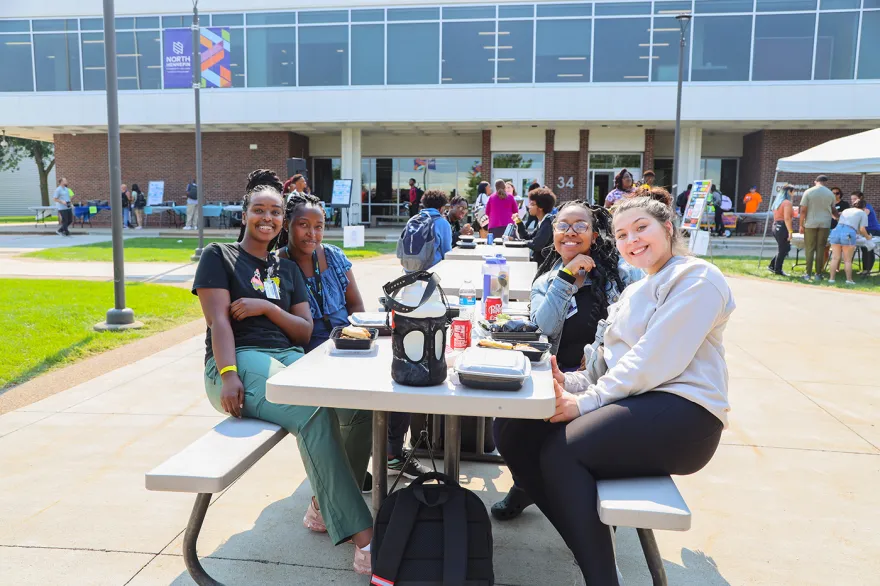 students sitting at an outdoor table smiling 
