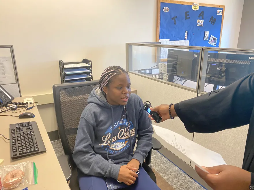 female student sitting at desk being interviewed