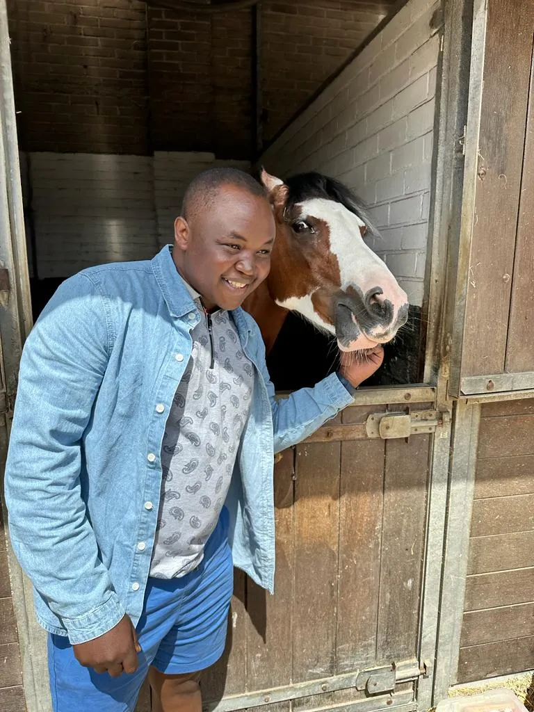 a photo of NHCC student, Donald Agik smiling next to a brown horse in the Dutch countryside
