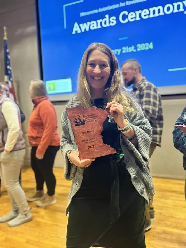 photo of Ana Munro smiling with an wooden award trophy shaped like Minnesota