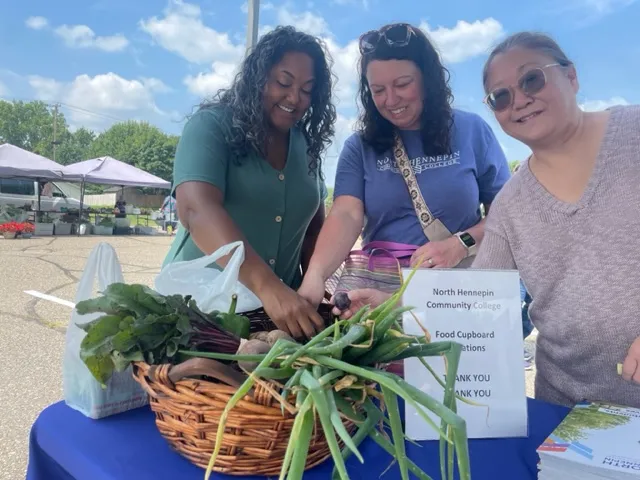 a photo of three NHCC staff members smiling while picking out produce at the Brooklyn Park Farmers Market 